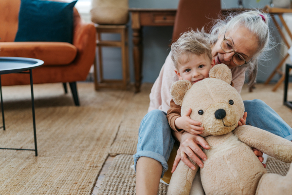 Grandmother cuddling her little grandson with a bear toy.