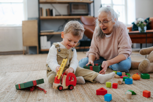 Grandmother playing with her little grandson, building a block set in his room.