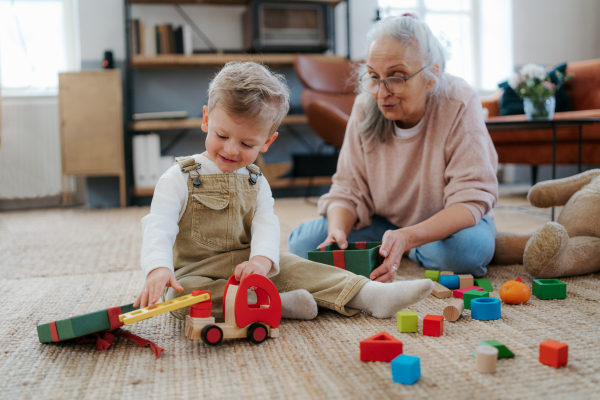 Grandmother playing with her little grandson, building a block set in his room.