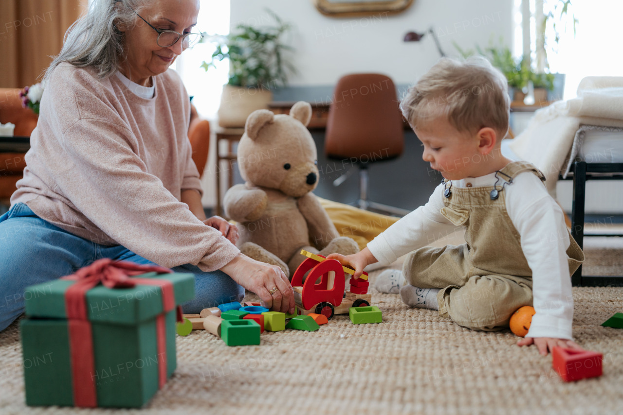 Grandmother playing with her little grandson and teddy bear. Playing with red wooden fire truck.