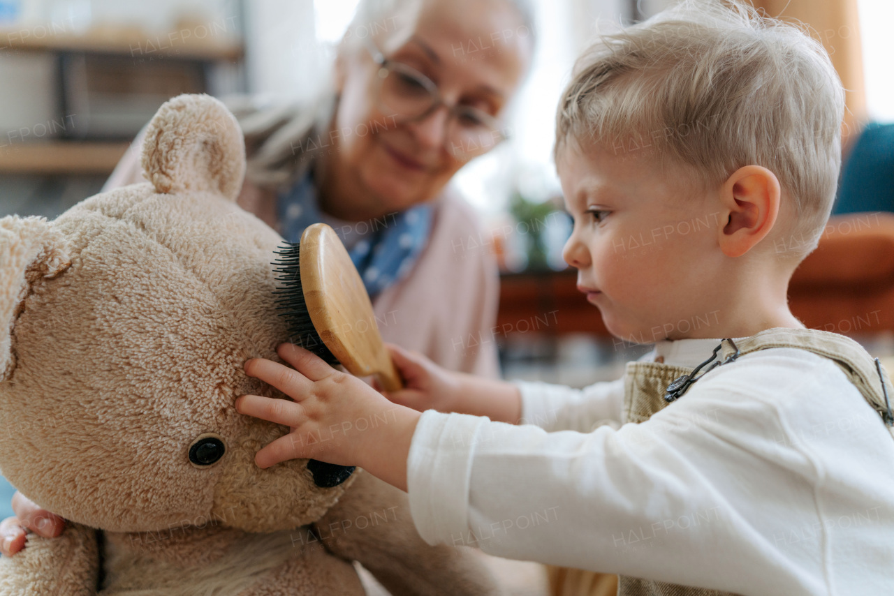 Little boy and grandmother take care of the stuffed toy. Child combing teddy bear's fur.