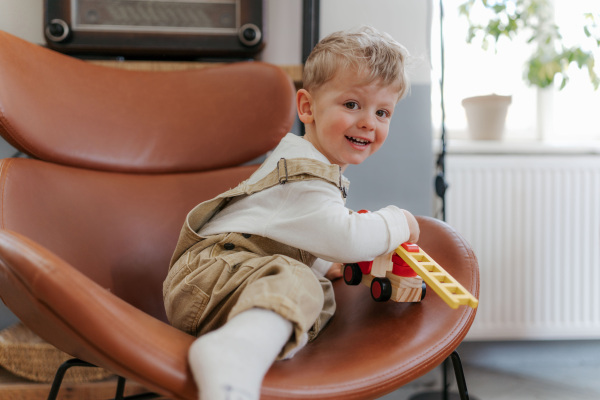 Happy little boy playing with red fire truck toy in the living room.