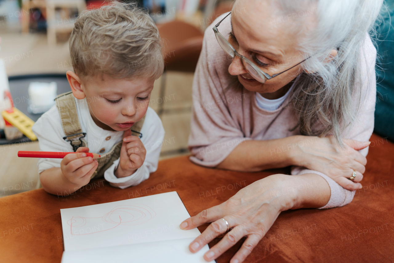 Grandson drawing in notepad with his grandmother. Little boy drawning with crayons.