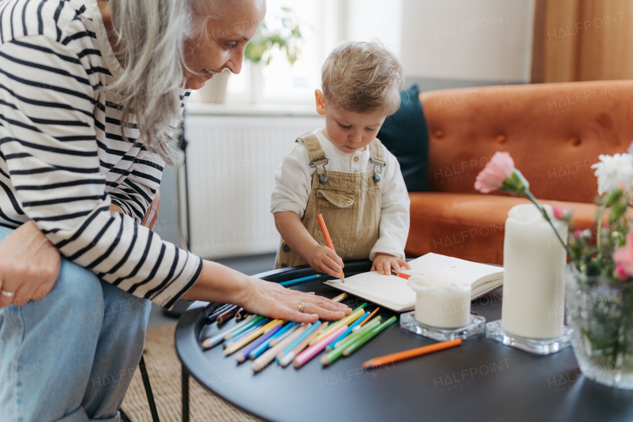 Grandson drawing in notepad with his grandmother. Little boy drawning with crayons.