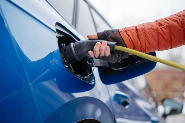 Close up of a charging electric car during cold snowy day, putting charger in charging port. Charging and driving electric vehicles during winter season.