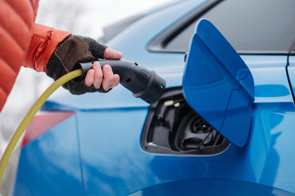 Close up of a charging electric car during cold snowy day, putting charger in charging port. Charging and driving electric vehicles during winter season.