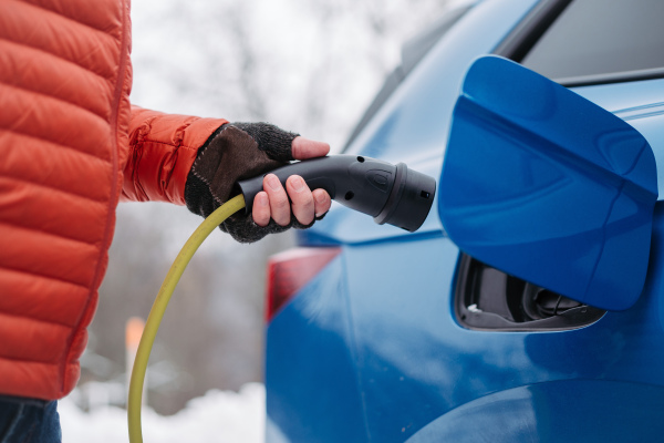 Close up of a charging electric car during cold snowy day, Charging and driving electric vehicles during winter season.