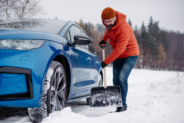 Man freeing his car stuck in the snow with shovel, getting car out from the snow drift. Scooping and throwing snow, shoveling.