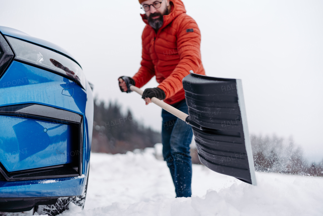 Man freeing his car stuck in the snow with shovel, getting car out from the snow drift. Scooping and throwing snow, shoveling.