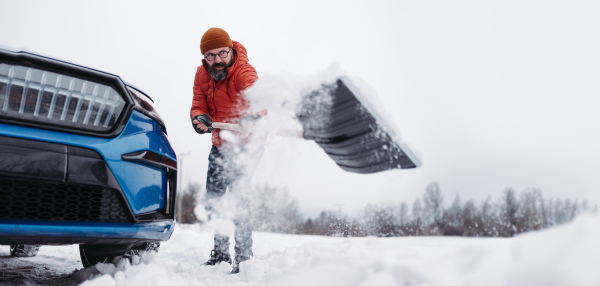 Man freeing his car stuck in the snow with shovel, getting car out from the snow drift. Scooping and throwing snow, shoveling. Winter banner with copy space.