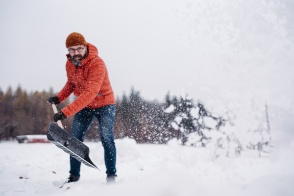 Man shoveling snow with shovel, cleaning driveway in front of his house. Scooping and throwing snow, shoveling.