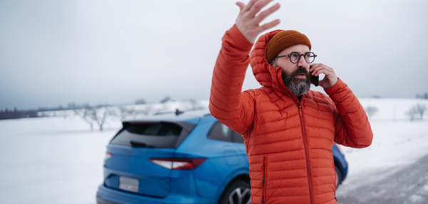 Angry man standing by electric car, battery run out of power before reaching destination. Man phone calling for help, waiting for the breakdown service car, tow truck.