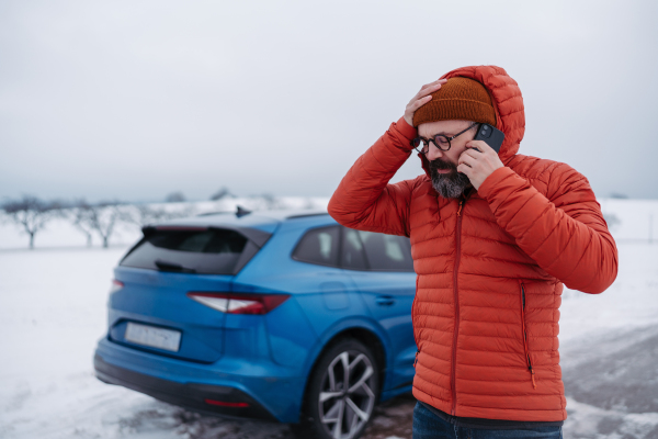 Angry man standing by electric car, battery run out of power before reaching destination. Man phone calling for help, waiting for the breakdown service car, tow truck.