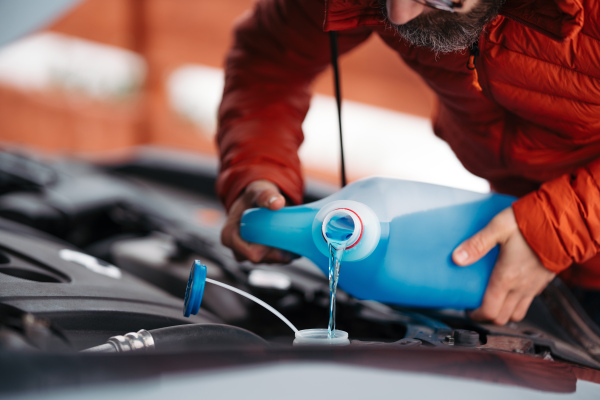 Pouring winter washer fluid into car reservoir during winter, protecting it from freezing. Concept of winter car care.