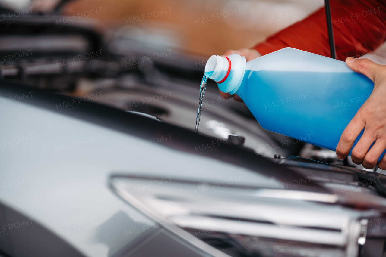 Pouring winter washer fluid into car reservoir during winter, protecting it from freezing. Concept of winter car care.