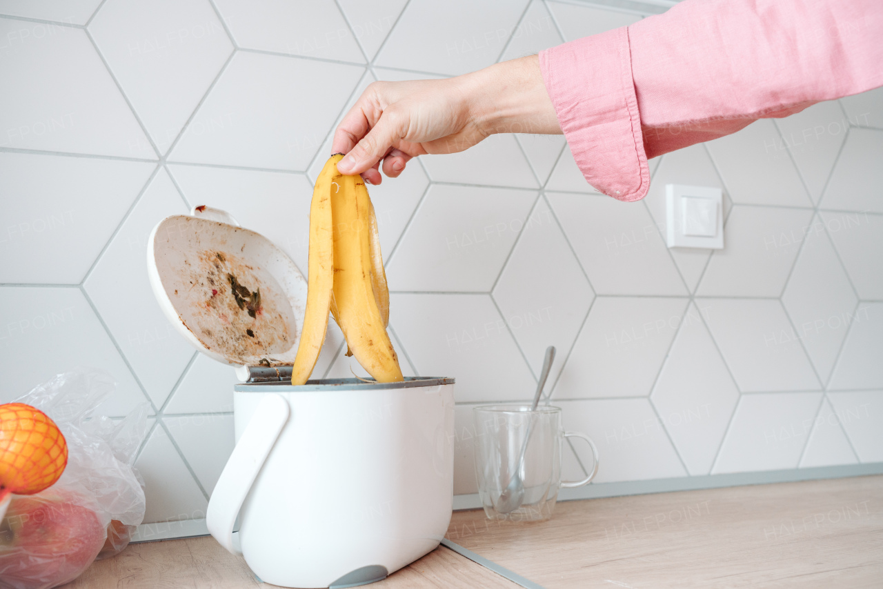 Man throwing banana peel into small countertop composter. Concept of home composting, converting kitchen biodegradable waste into compost at home.