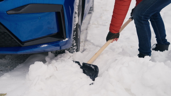 Man freeing his car stuck in the snow with shovel, getting car out from the snow drift. Scooping and throwing snow, shoveling.