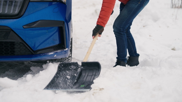 Man freeing his car stuck in the snow with shovel, getting car out from the snow drift. Scooping and throwing snow, shoveling.