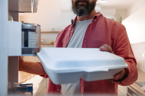 Handsome man putting lunchbox, takeaway container in fridge. Taking out lunch from fridge, eating leftovers. Do not trow food away, reducting food waste.