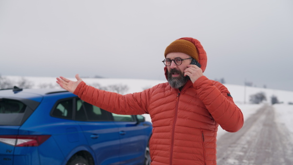 Angry man standing by electric car, battery run out of power before reaching destination. Man phone calling for help, waiting for the breakdown service car, tow truck.