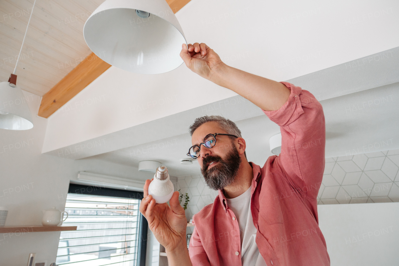 Man changing LED bulbs at home. Concept of energy efficiency, longevitiy and environmental impact of an electronic bulb.