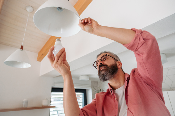 Man changing LED bulbs at home. Concept of energy efficiency, longevitiy and environmental impact of an electronic bulb.