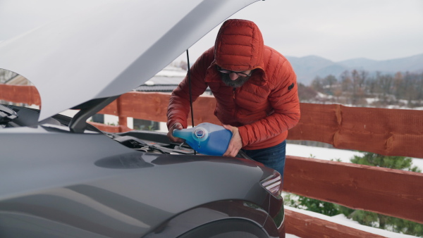 Pouring winter washer fluid into car reservoir during winter, protecting it from freezing. Concept of winter car care.