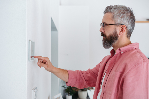 Man using smart thermostat, adjusting or lowering heating temperatures at his home. Concept of sustainable, efficient, and smart technology in home heating and thermostats.