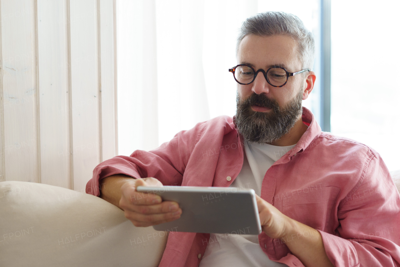 Man using smart thermostat, adjusting, lowering heating temperature at home. Man watching tv show on tablet, video streaming services with movies and tv shows online.