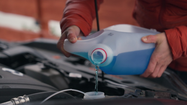 Pouring winter washer fluid into car reservoir during winter, protecting it from freezing. Concept of winter car care.