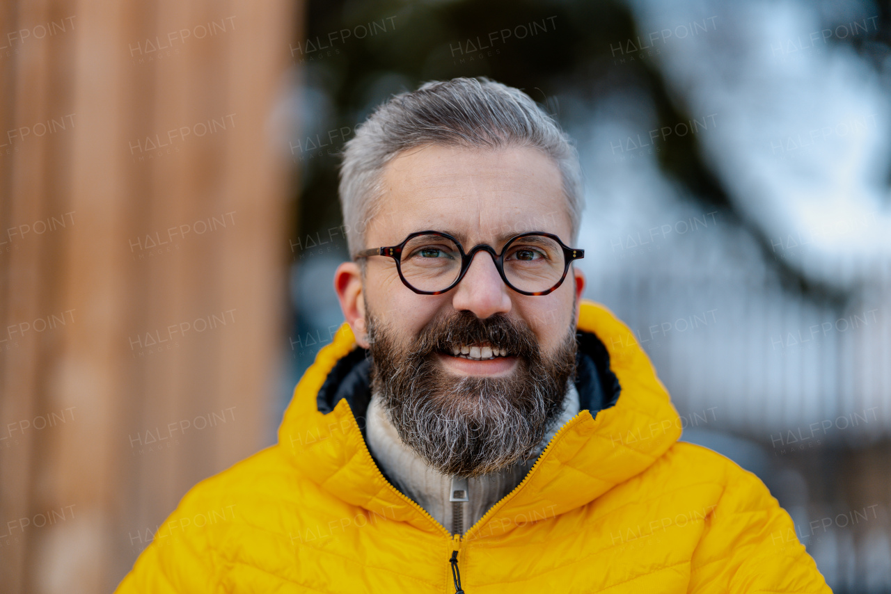 Portrait of man standing on cabins patio, looking at camera, smiling. Handsome man spending relaxing, stress-free winter weekend in cabin in mountains.