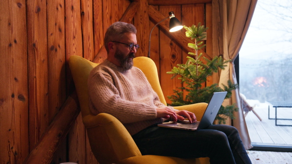 Mature man working in cabin on laptop. Concept of remote work from home. Hygge at work.