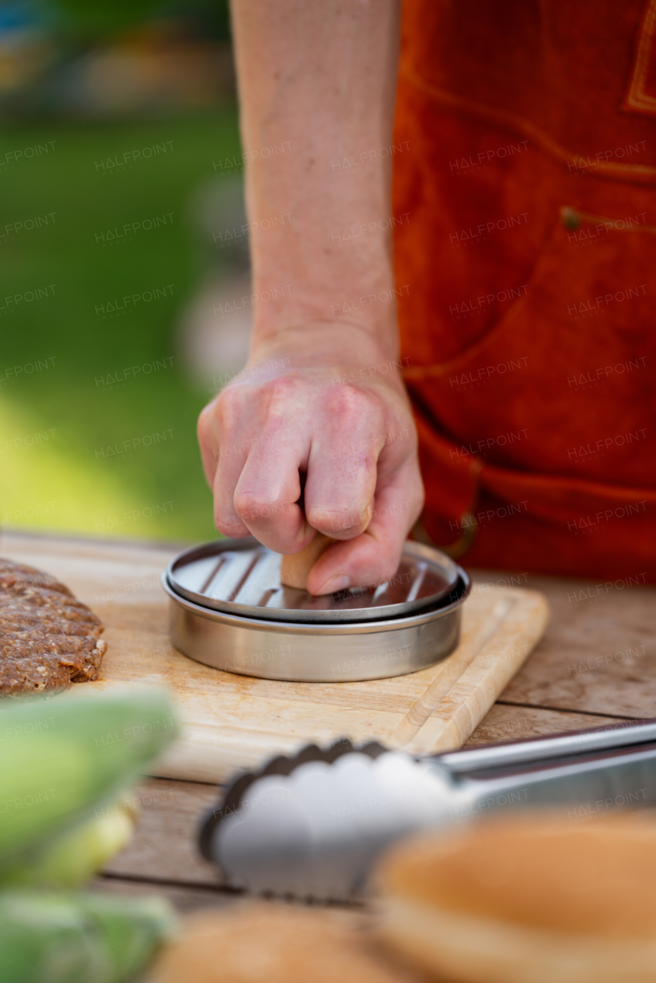 Man in apron preparing meat for hamburgers, standing outdoors. Using burger press to shape groud meat.