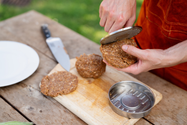 Man in apron preparing meat for hamburgers, standing outdoors. Using burger press to shape groud meat.