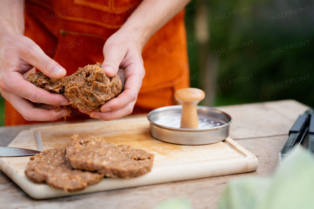 Man in apron preparing meat for hamburgers, standing outdoors. Using burger press to shape groud meat.