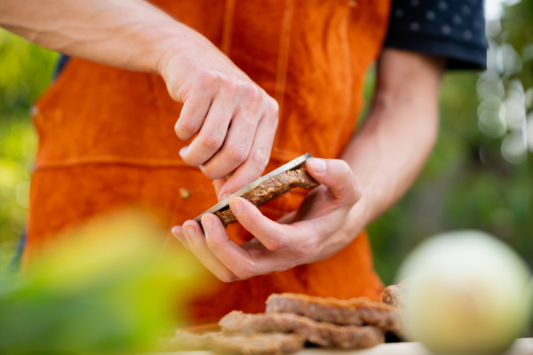 Man in apron preparing meat for hamburgers, standing outdoors. Using burger press to shape groud meat.