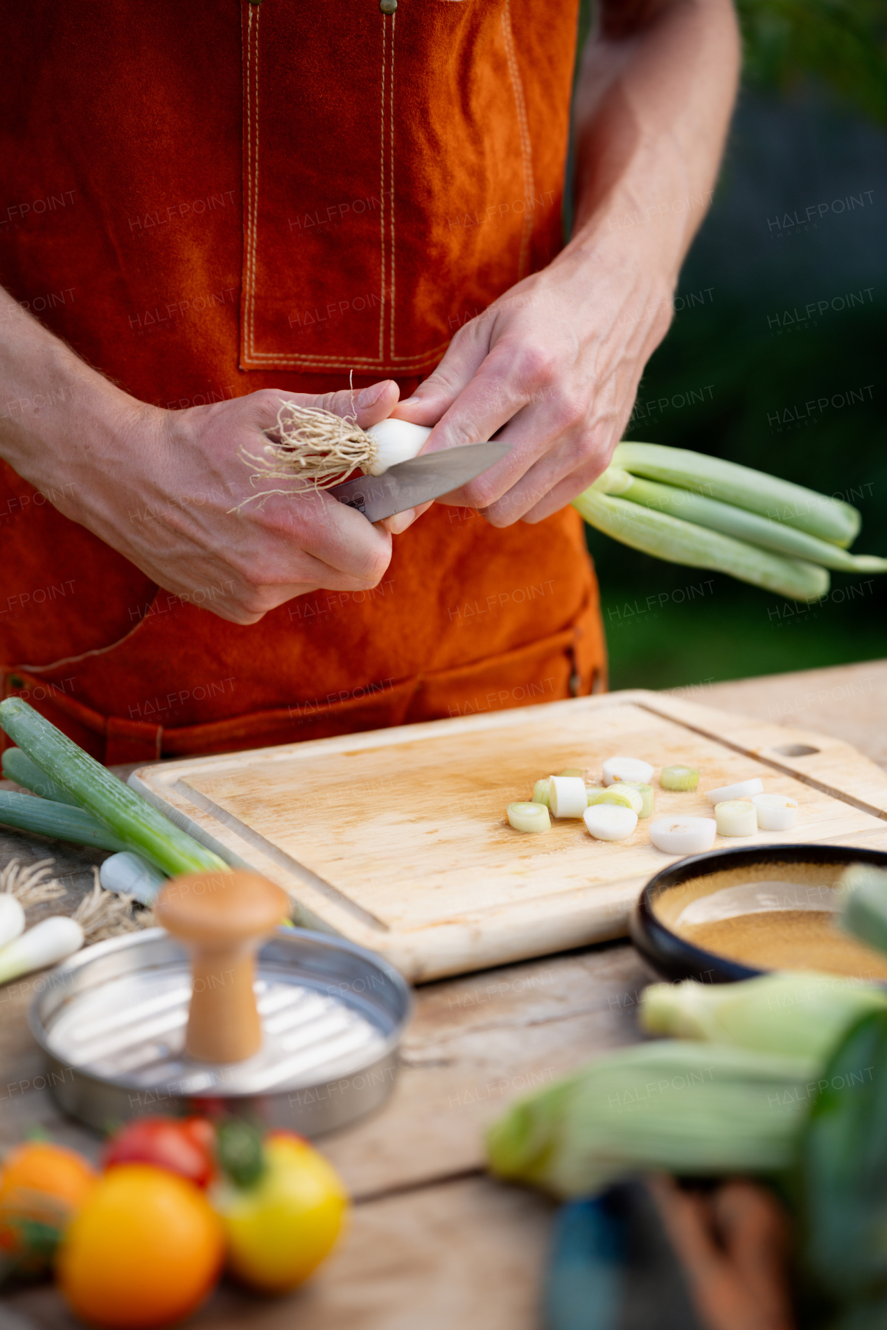 Close up of man holding sharp knife, peeling spring green onion. Preparing vegetables for an outdoor barbecue.