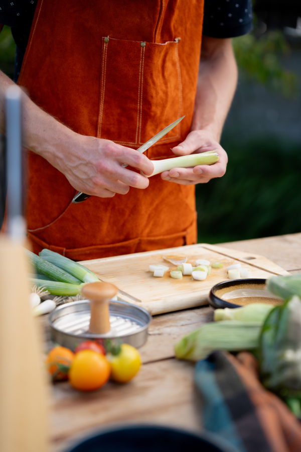 Close up of man holding sharp knife, peeling spring green onion. Preparing vegetables for an outdoor barbecue.