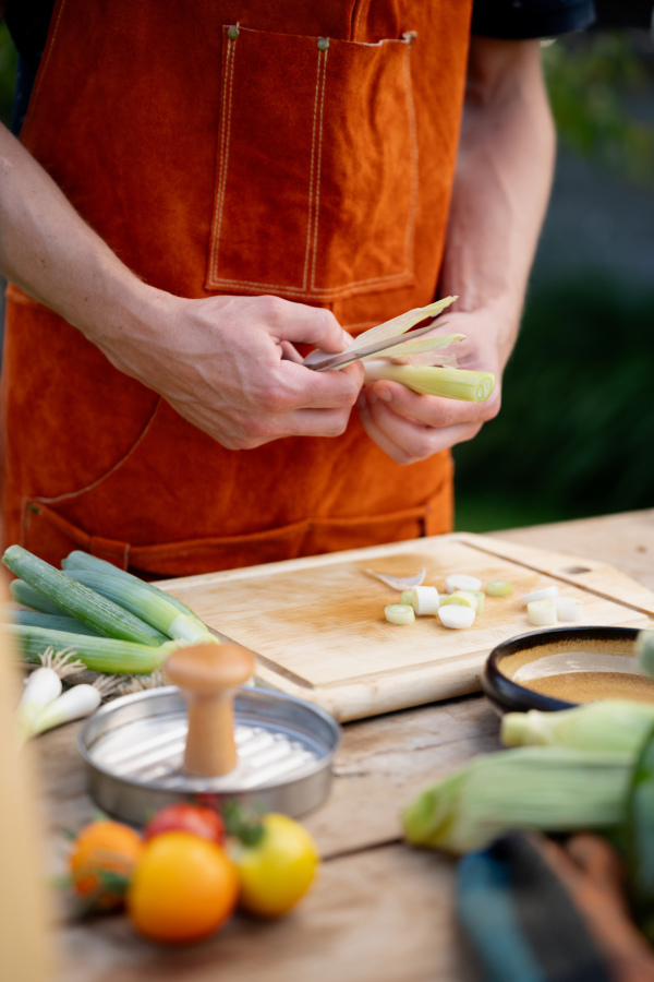 Close up of man holding sharp knife, peeling spring green onion. Preparing vegetables for an outdoor barbecue.