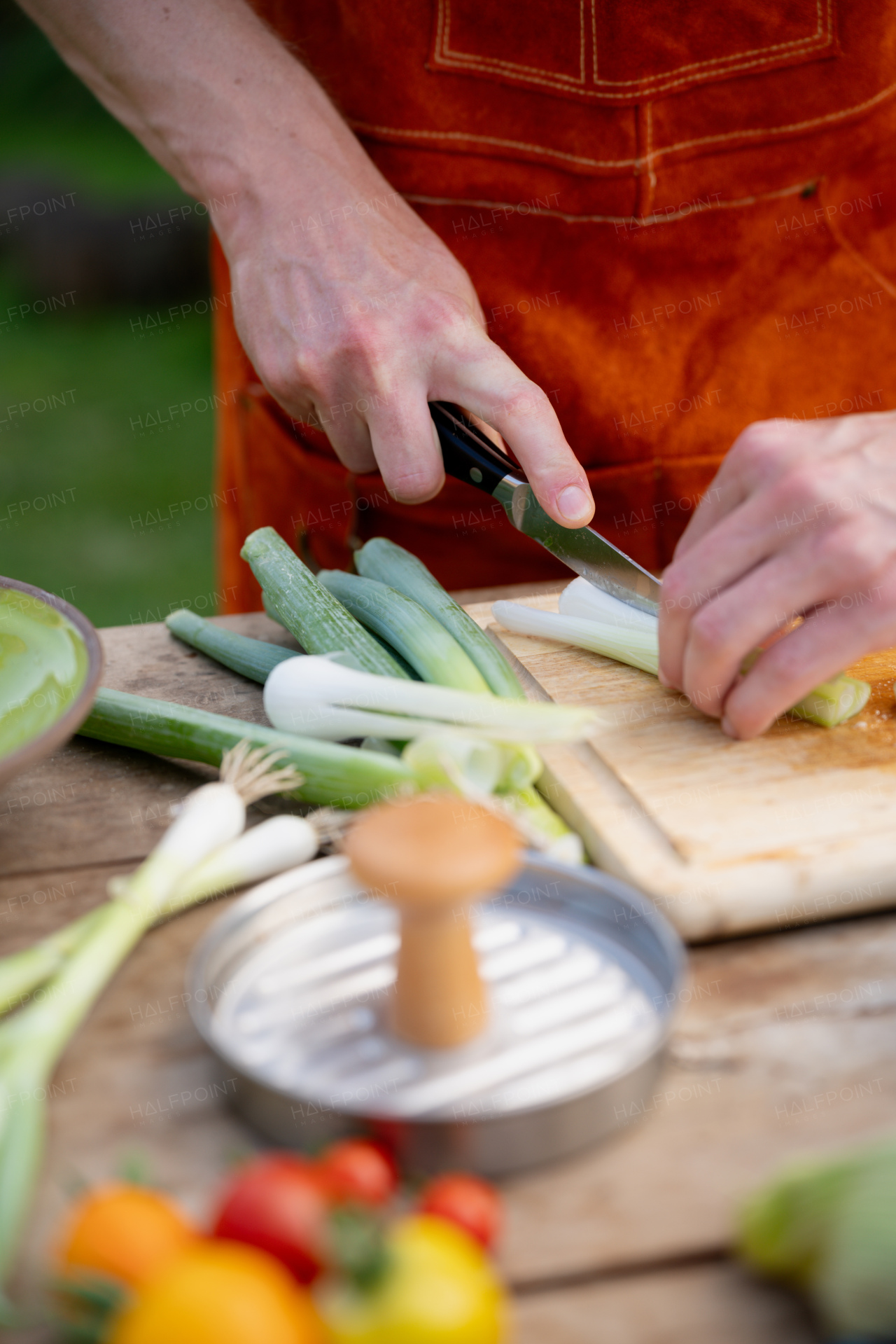 Close up of man holding sharp knife, cutting spring green onion. Preparing vegetables for an outdoor barbecue.