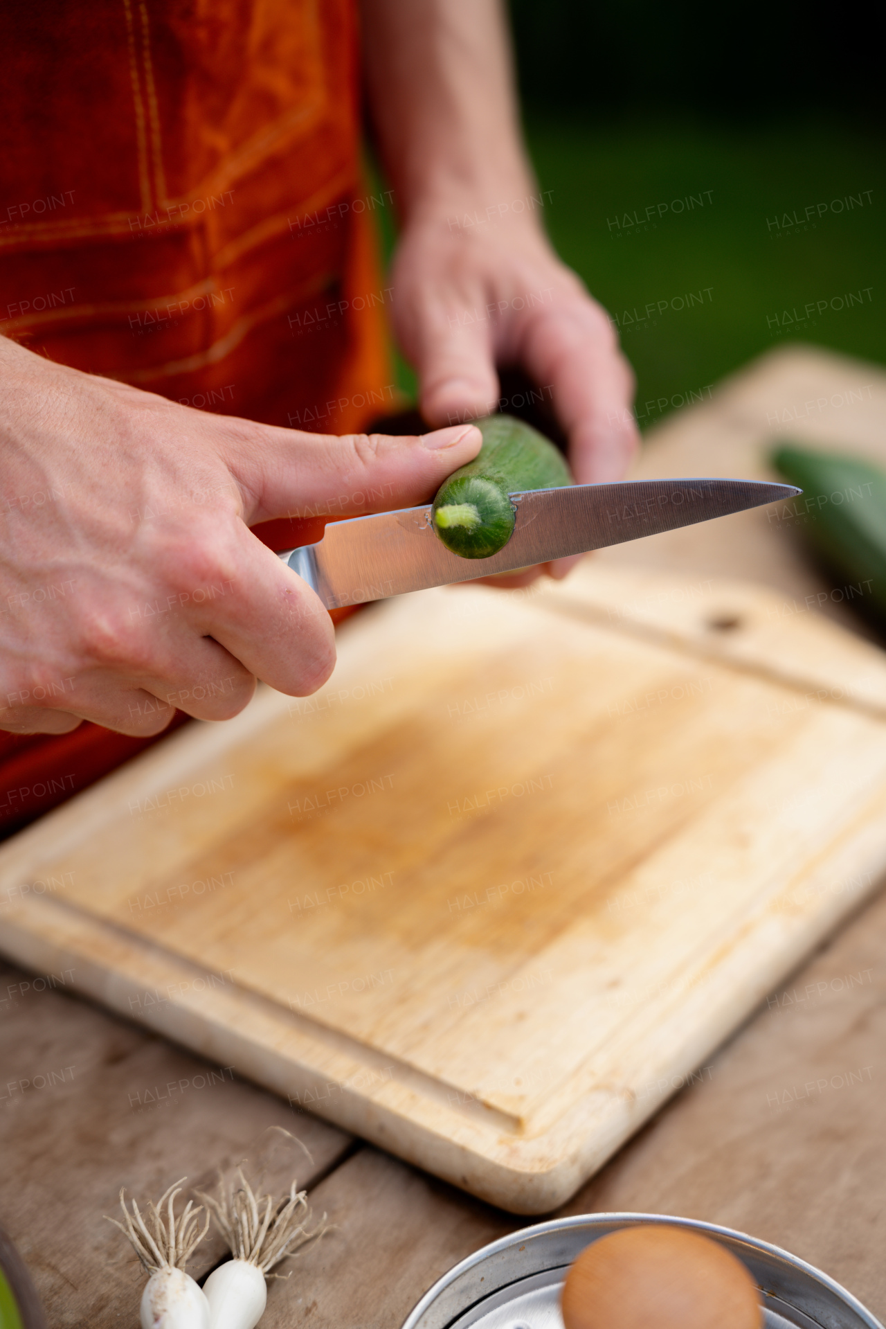 Close up of man holding sharp knife, peeling salad cucumber. Preparing vegetables for an outdoor barbecue.