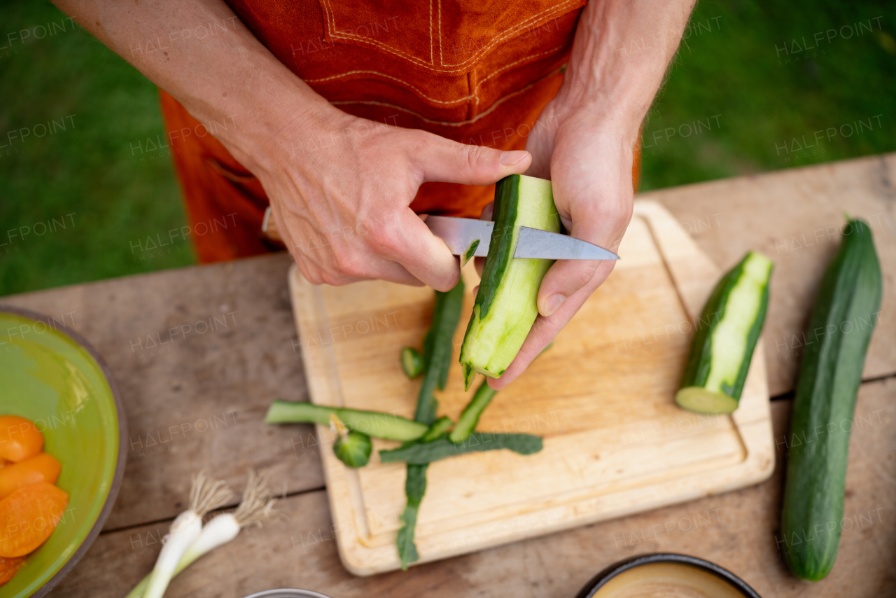 Close up of man holding sharp knife, peeling salad cucumber. Preparing vegetables for an outdoor barbecue.