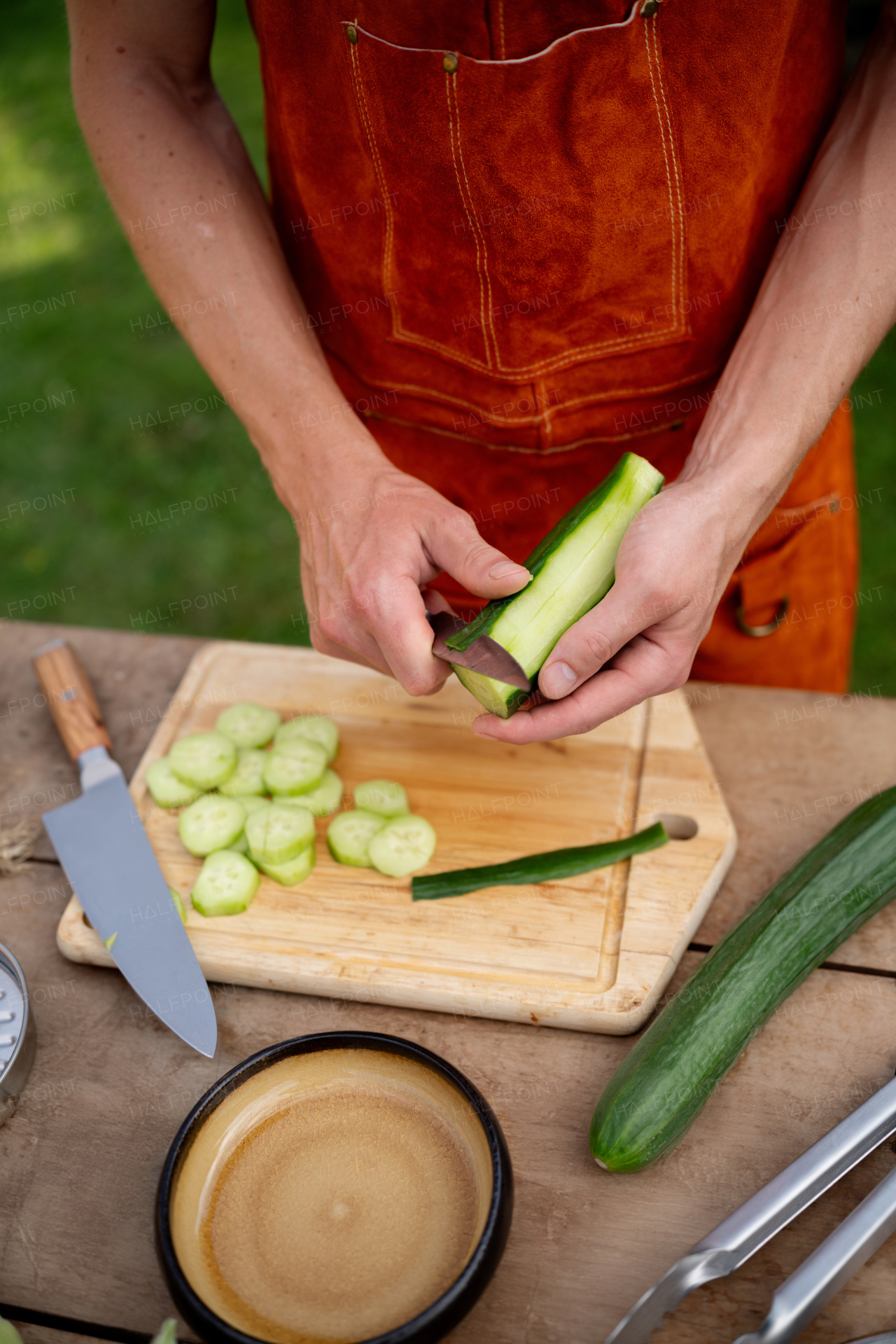 Close up of man holding sharp knife, peeling salad cucumber. Preparing vegetables for an outdoor barbecue.