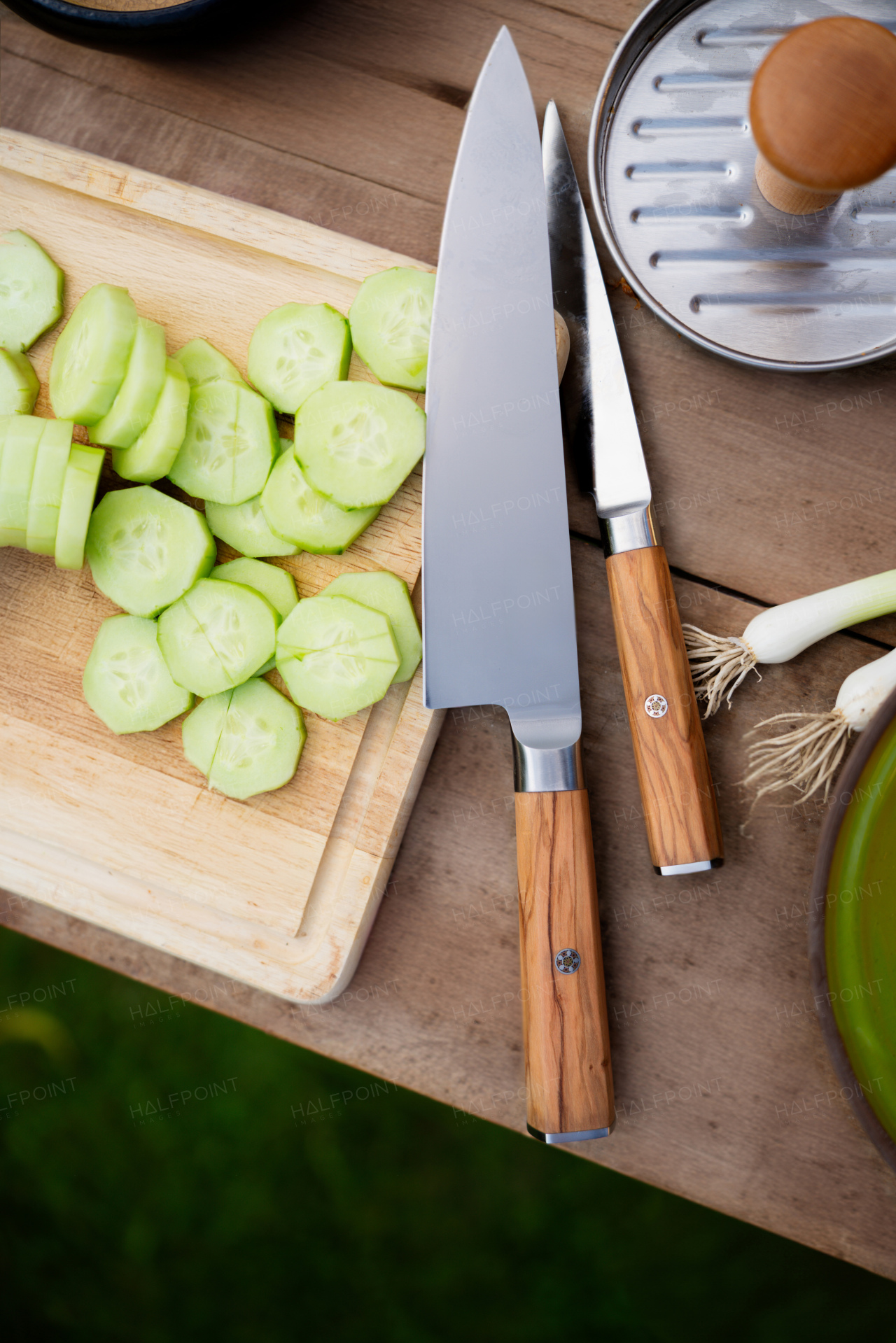 Top view of cutting board with sharp knifes, chopped cucumber and burger patty press.