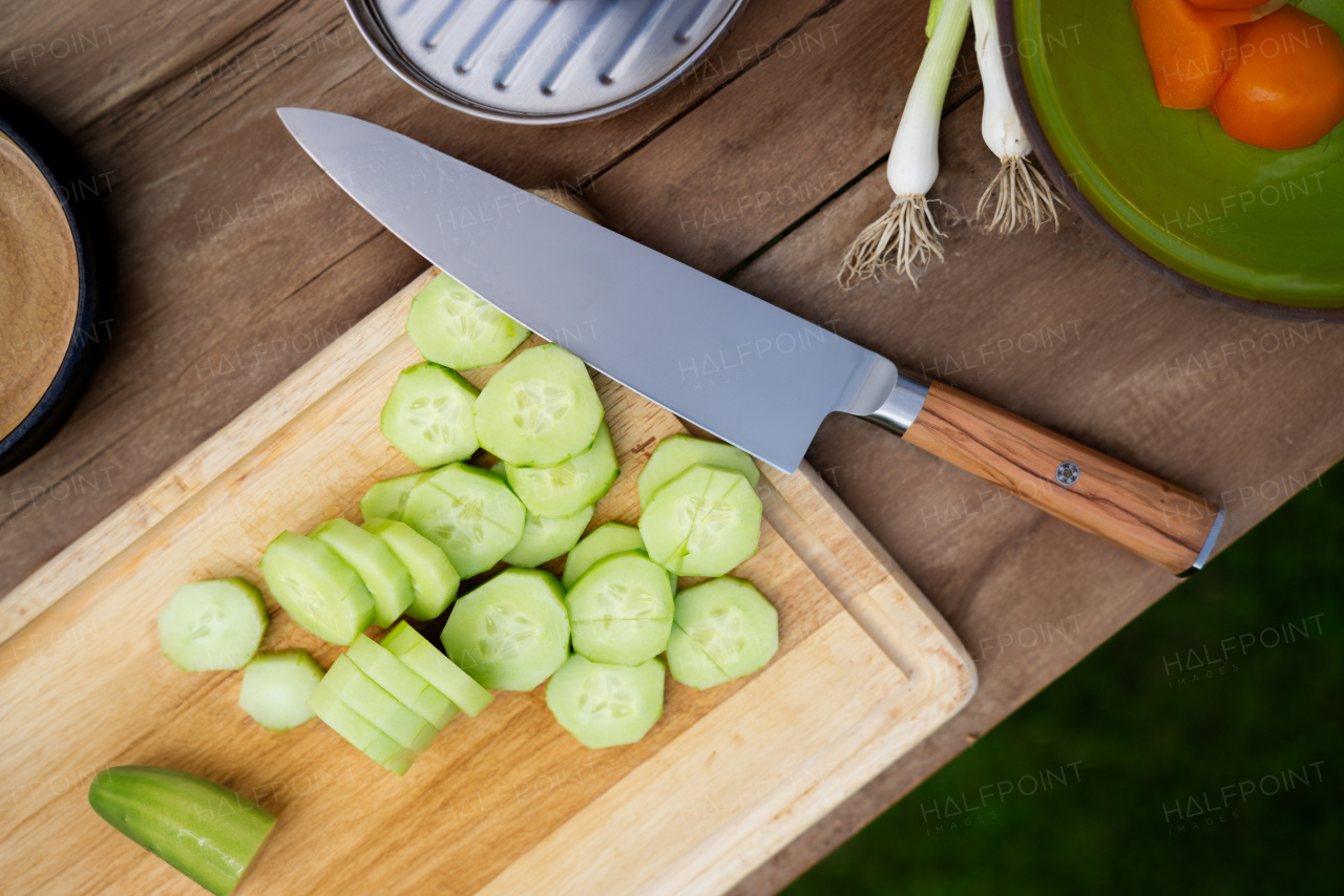 Sharp knife and chopped cucumber on cutting board. Preparing vegetables for outdoor barbecue.