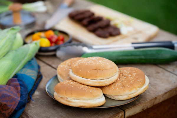 Preparing food for an outdoor barbecue. Hamburger buns on tablet vegetables and grilled burger patties