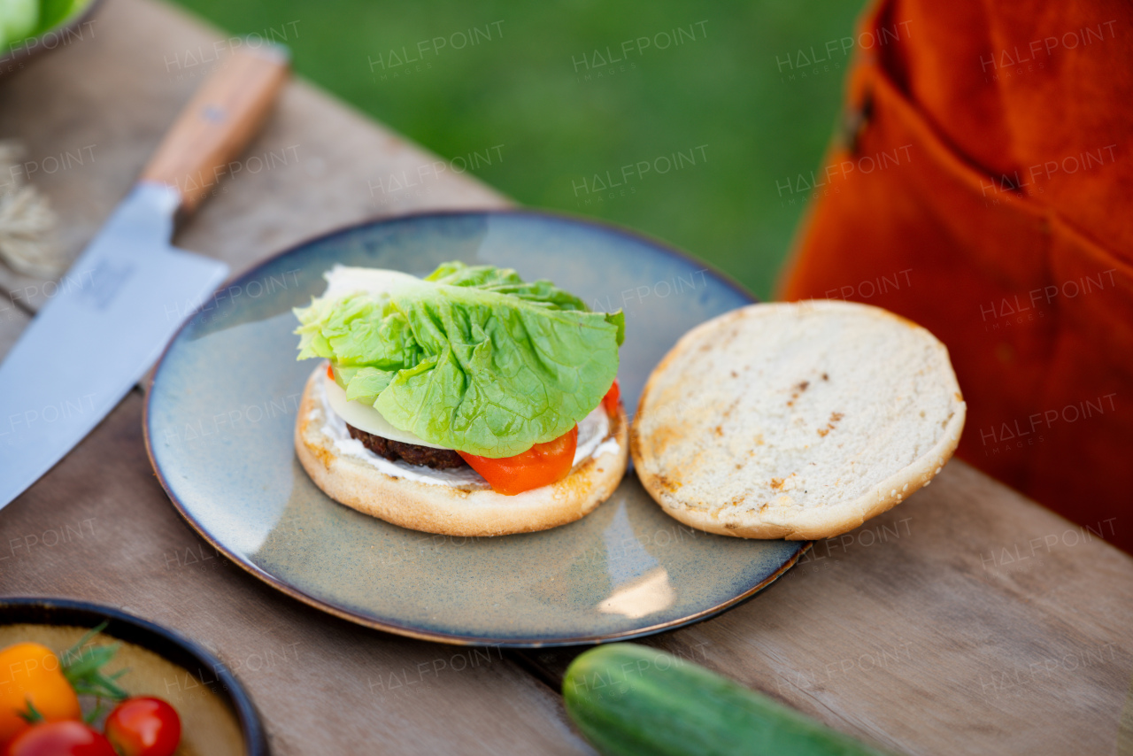 Close up of man assembling burgers with toppings, putting toasted bun on top of hamburger.