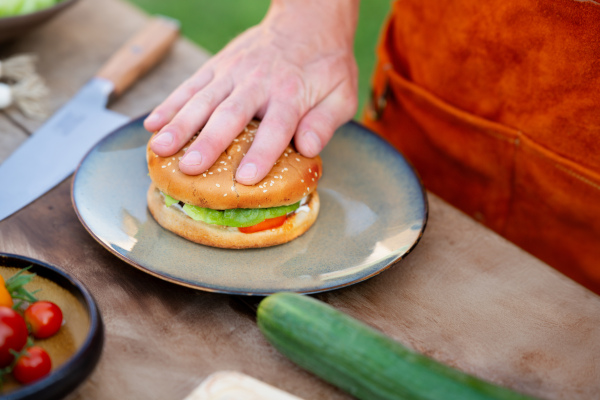 Close up of man assembling burgers with toppings, putting toasted bun on top of hamburger.