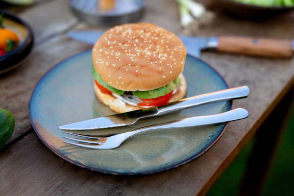 Close up of plate with homemade grilled hamburger and cutlery.