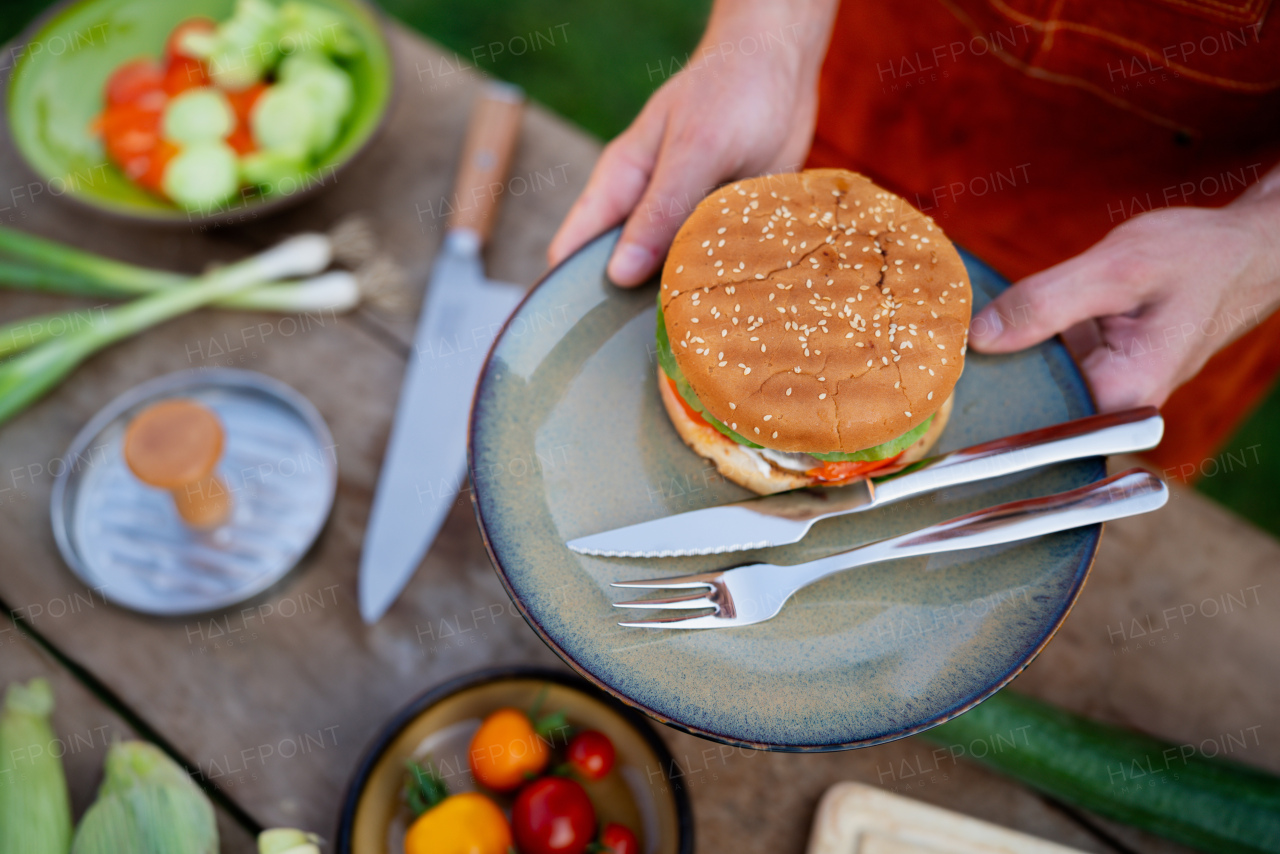 Close up of man holding plate with homemade grilled hamburger and cutlery.